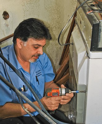 An Allstar technician in a branded shirt repairing an appliance