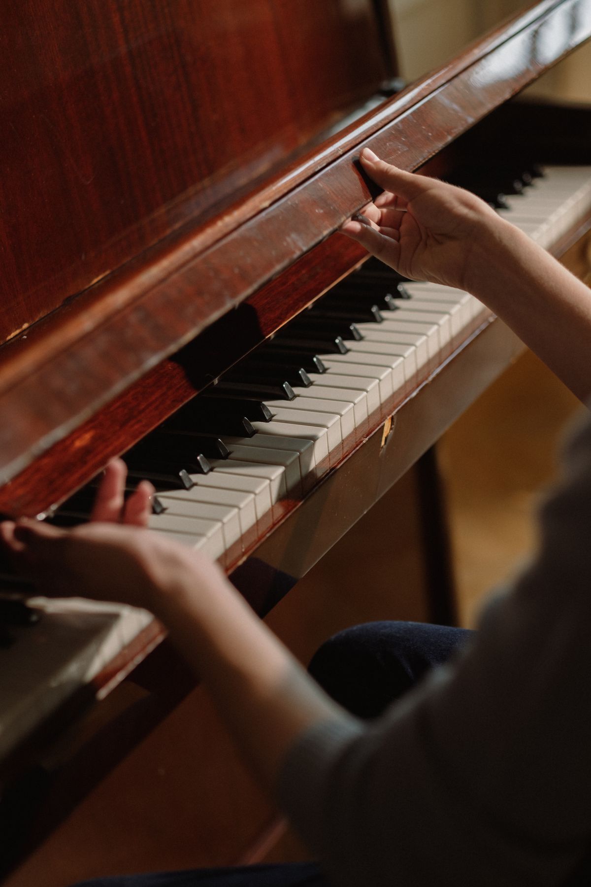 Warm close-up of hands at a mahogany upright piano